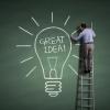 Man on ladder drawing light bulb on big blackboard